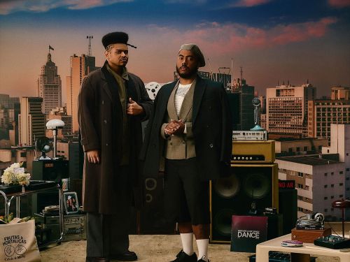 Imagem de dois homens vestido socialmente, com o fundo de uma cidade