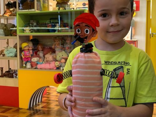 um menino de blusa verde segurando um brinquedo dentro do acervo do museu dos brinquedos 