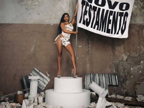 Imagem com uma mulher em pé segurando uma bandeira com o nome do disco 