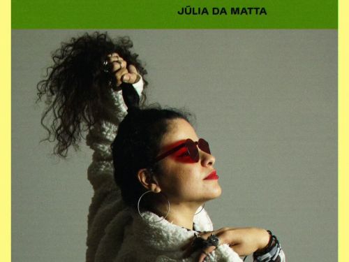 Mulher segurando o cabelo preso com óculos escuro e blusa de frio branca com manga xadrez