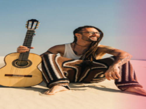 Foto mostra um homem sentado na praia segurando um violão