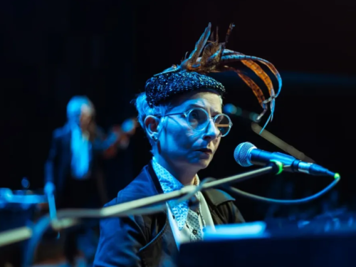 uma mulher 60+ com um chapéu com pena e traje elegante sentada em uma piano 