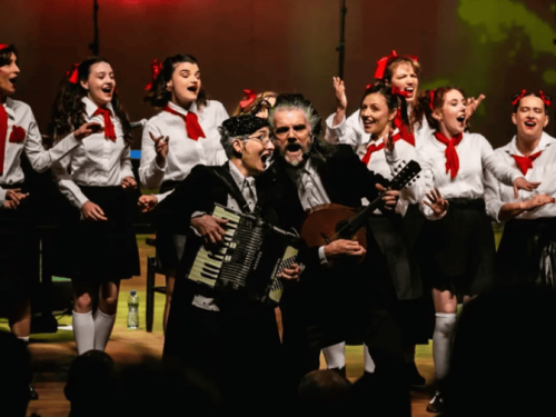 um home e uma criança tocando e cantando com muitas cantoras ao fundo