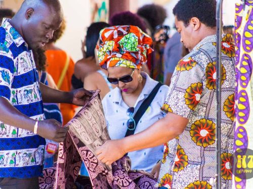 Foto de três pessoas negras com roupas e adereços afro, manuseando tecido em estampa afro.