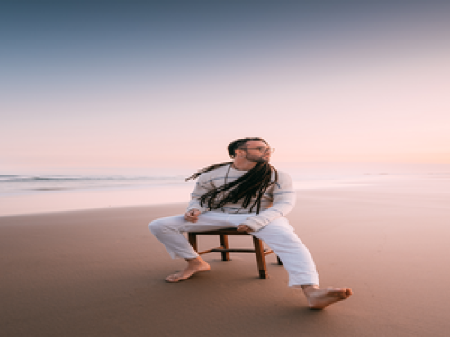 Foto mostra um homem sentado em um banquinho na areia da praia