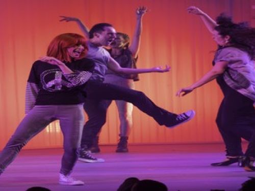 Atriz Mel Lisboa vestida como e interpretando Rita Lee, acompanhada de bailarinos