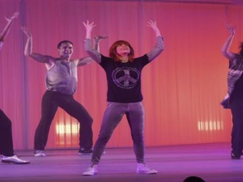 Atriz Mel Lisboa vestida como e interpretando Rita Lee, acompanhada de bailarinos