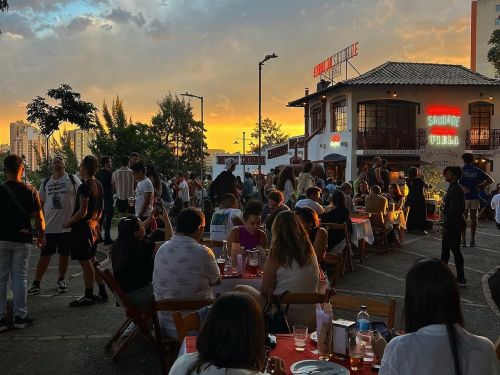 Imagem do local, praça ao ar livre ao por do sol com pessoas ocupando o espaço