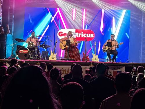 Imagem de três pessoas caracterizadas de pessoas mais velhas, em um palco, tocando instrumentos 