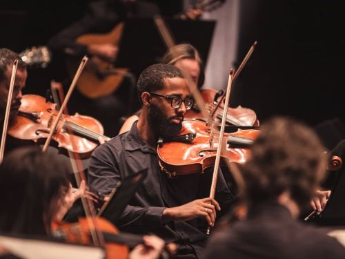 A foto mostra o foco em um violinista da orquestra ouro preto tocando.