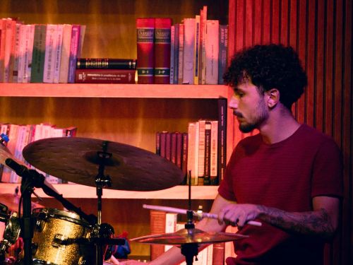 um homem tocando bateria com luzes rosa e vermelha ao fundo