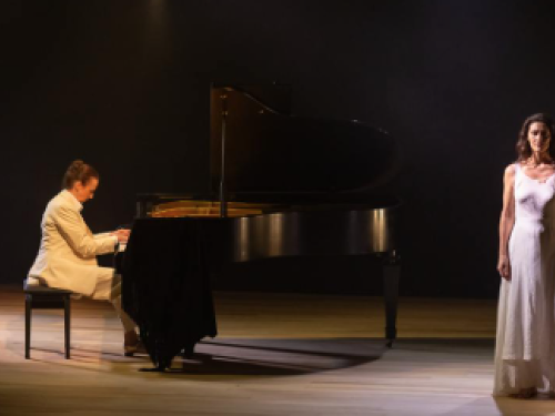 Imagem de uma mulher tocando piano e uma mulher em pé ao lado com o vestido branco