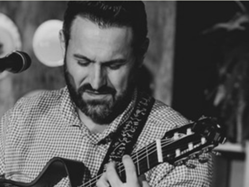 Imagem preta e branca, com um homem tocando um instrumento com um microfone na sua frente