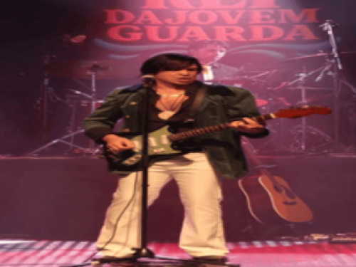 Imagem deu banda tocado, em destaque um homem tocando guitarra com o microfone na sua frente