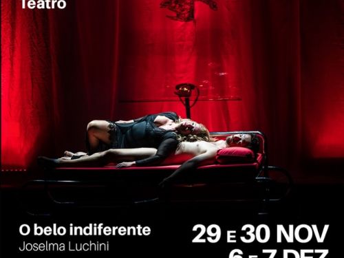 Espetáculo: "O Belo Indiferente" - Cena teatral iluminada por luz vermelha intensa. Uma mulher está deitada sobre um homem em uma cama metálica, em um momento de forte carga dramática. Ao fundo, cortinas vermelhas e uma escultura pendurada compõem o cenário.