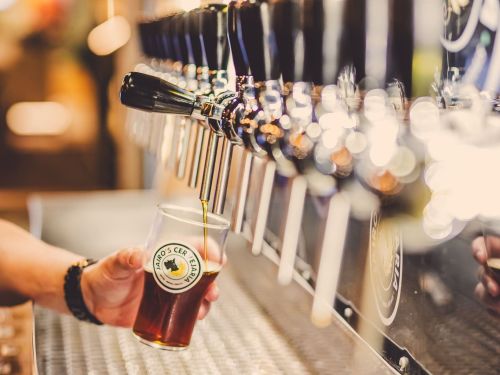 Imagem de varias torneiras de chopp, e uma pessoa enchendo o copo de chopp