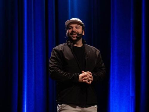 A imagem mosta o artista comediante Raphael Ghanem no palco com o fundo azul
