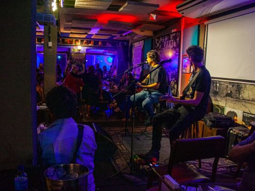 Imagem do espaço, cantores no palco e luzes baixas.