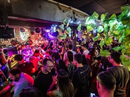 A foto mostra a pista do estabelecimento jangal, com letreiros luminosos nas paredes e pessoas ocupando o espaço 