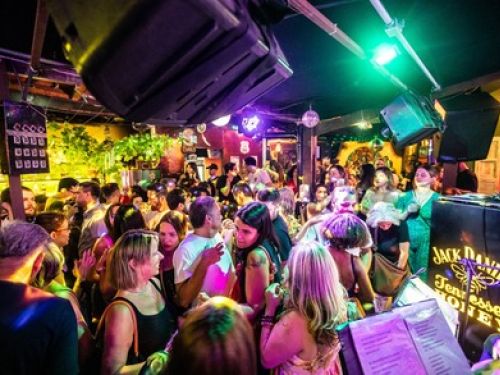 A foto mostra a pista do estabelecimento jangal, com letreiros luminosos nas paredes e pessoas ocupando o espaço 