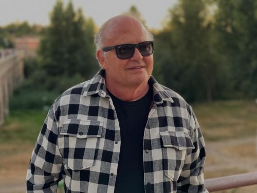 Imagem de um homem sorrindo, de óculos escuros, ao ar livre.