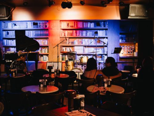 Foto do espaço interno do local, com luz baixa, estantes e mesas