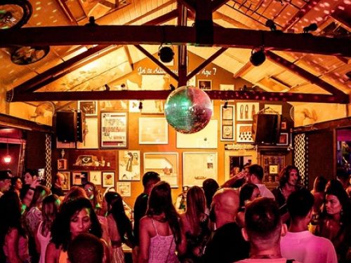 Imagem do interior do espaço, pista de dança cheia e globo de festa.