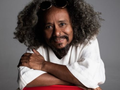 Imagem real de Chico Cesár posando para foto em cima de uma cadeira vermelha 