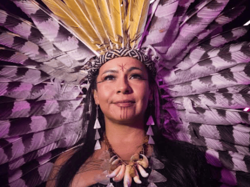 Imagem de uma mulher indígena, com um cocar e colares. 