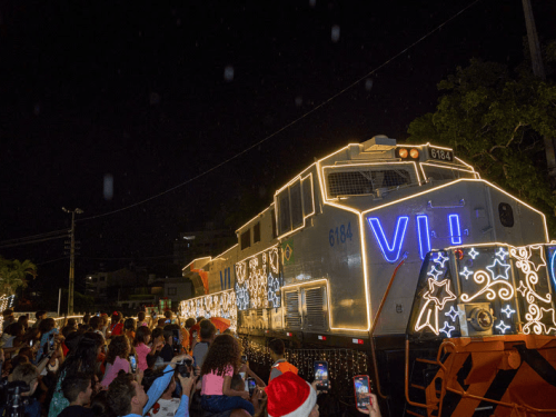 Imagem com um trem iluminado, e varias pessoas em volta. 