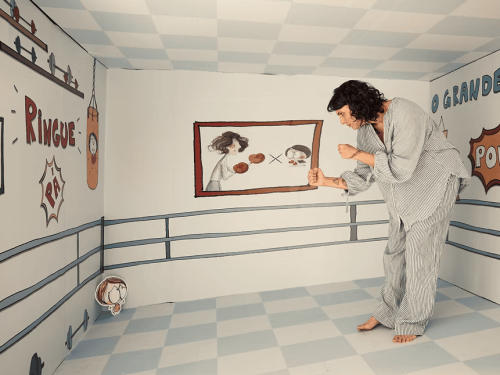 Imagem de uma mulher em um quarto desenhado, com um desenho de uma criança, simulando uma "luta"