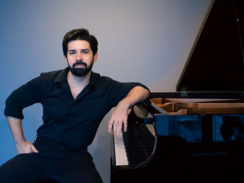 Fotografia do artista João Pedro Vasconcelos tocando piano, com fundo azul.