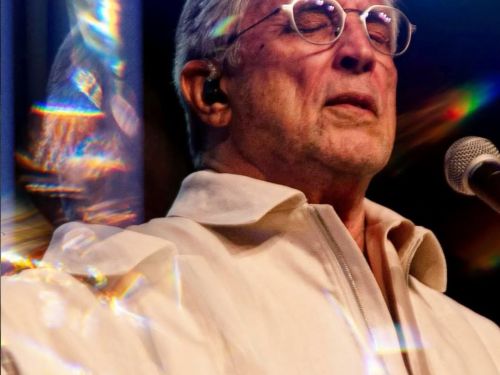 Imagem de um homem de cabelos grisalhos e óculos cantando de olhos fechados 