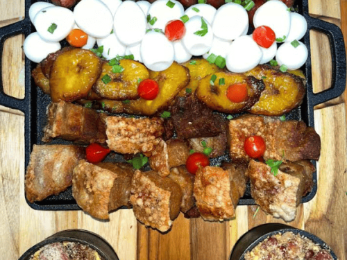 Esta imagem apresenta uma chapa de ferro retangular repleta de petiscos típicos da culinária mineira, organizada em camadas horizontais coloridas.