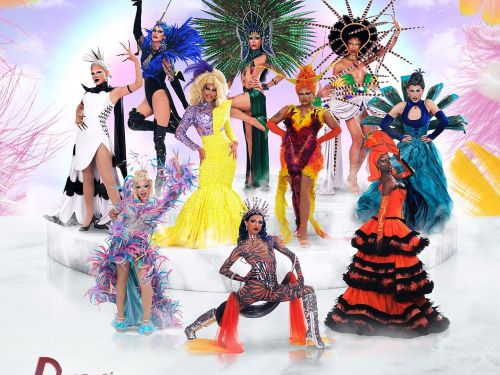 O cartaz apresenta o elenco de Drag Race Brasil posando em uma estrutura circular branca que lembra degraus de mármore. O fundo é composto por um céu azul com nuvens suaves, emoldurado por grandes penas coloridas em tons de rosa, laranja e amarelo.
