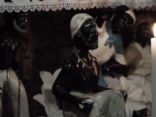 Miniatura de orixás com vestimentas brancas, colares e acessórios na cabeça. Filme "Fé e Fúria".