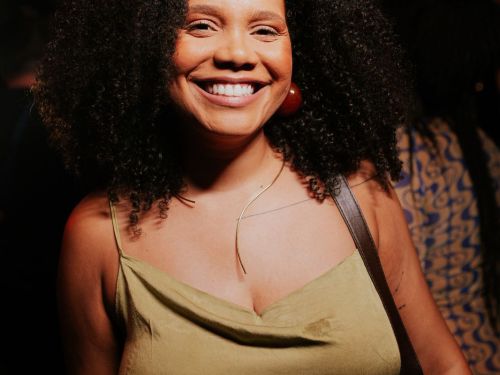 Uma mulher preta cis de cabelo cacheado volumoso com um vestido verde musgo