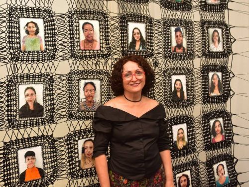 Foto da artista Marlene Barros na frente de uma de suas obras 