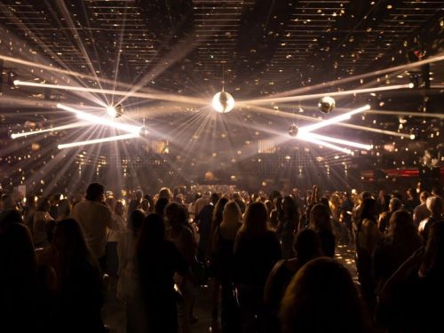 Multidão em casa de show, ambiente iluminado com jogo de luzes brancas.