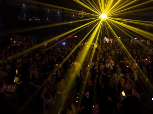 Multidão em casa de show, ambiente iluminado com jogo de luzes amarelas.