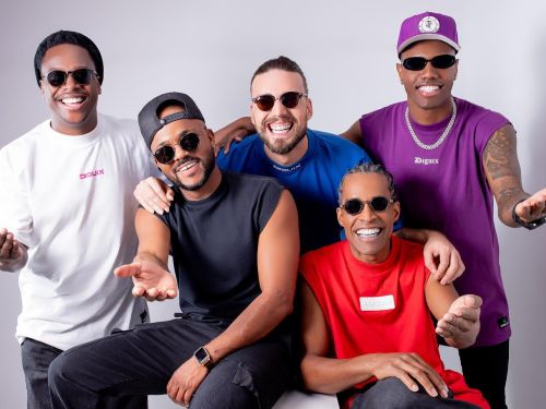 Artistas do Grupo Simplicidade Samba. Cinco homens posando para foto sorrindo. Usam roupas coloridas, há três homens sentados e dois em pé. Foto sob fundo cinza.