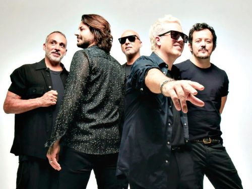 Foto do grupo musical Jota Quest. Cinco homens usando roupas escuras e fazendo pose para a foto. Dois homens usam óculos escuro. Imagem com fundo branco.