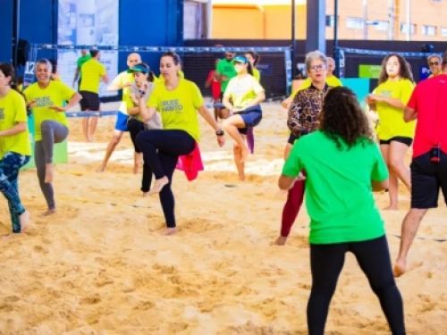 Grupo de pessoas fazendo aquecimento em uma quadra de areia 