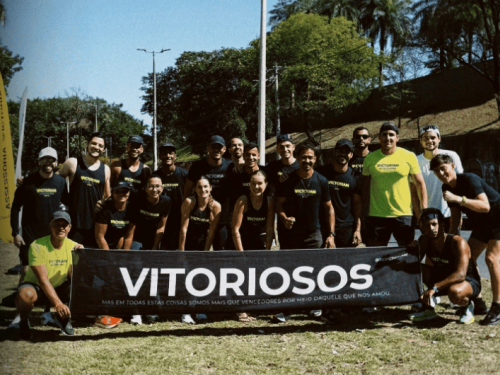 Grupo de corredores segurando faixa preta com o nome da corrida "Vitoriosos"
