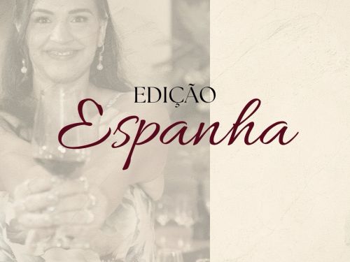 Card promocional anunciando a "EDIÇÃO Espanha". A imagem é dividida verticalmente: o lado esquerdo traz a fotografia desbotada e em tons neutros de uma mulher sorridente em um vestido estampado, estendendo uma taça de vinho em direção à câmera; o lado direito apresenta um fundo texturizado em tom creme com uma linha fina na base. Centralizado entre as duas metades, destaca-se o texto "EDIÇÃO" em letras maiúsculas finas e, logo abaixo, a palavra "Espanha" escrita em uma fonte cursiva elegante na cor vinho.