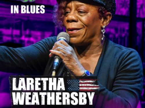 O cartaz do show Rota do Blues apresenta uma identidade visual marcante dominada por uma forte iluminação em tons de roxo e neon ao fundo. No centro da peça publicitária, destaca-se a fotografia em plano médio da cantora Laretha Weathersby, que aparece sorrindo de forma expressiva enquanto segura um microfone com a mão direita próximo ao rosto. Ela veste um casaco escuro sobre uma blusa preta, usa brincos compridos prateados em formato de clave de sol e uma boina preta brilhante com detalhes em strass na ab
