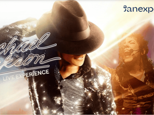 Banner horizontal com fundo de luzes azuis e douradas destaca um sósia de Michael Jackson em duas poses de show: no centro, sorrindo de perfil com chapéu fedora preto e jaqueta de lantejoulas brilhantes; à direita, ao fundo, cantando ao microfone. No lado esquerdo, lê-se em letras cursivas e luminosas "Michael Jackson - LIVE EXPERIENCE". No canto superior direito está a marca "sanexperience" e, no canto inferior esquerdo, um detalhe rosa-choque.