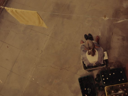 PERSPECTIVA SOLIDÃO. Foto tirada de cima de uma senhora sentada no quintal de casa 