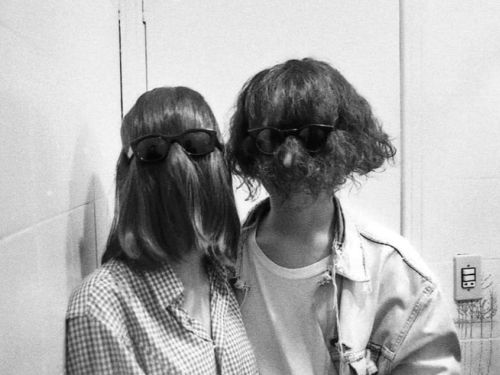 Foto de um homem e uma mulher com o cabelo tampando a cara enquanto usam óculos escuro 