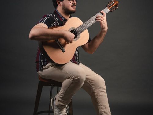 Foto do cantor Octávio Deluchi sentado enquanto toca um violão 